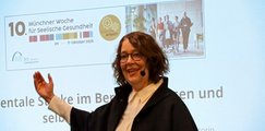 Frau hält stehend einen Vortrag vor einer Leinwand mit Präsentation