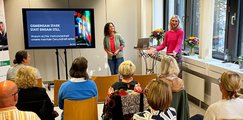Zwei Frauen stehen vorn auf der Bühne neben Bildschirm