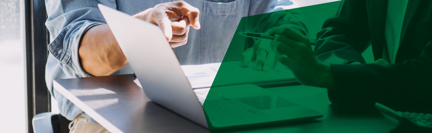 Header: Meeting mit zwei Personen und einem Laptop auf dem Tisch. Die Hand des Mannes zeigt auf den Bildschirm des Laptop.