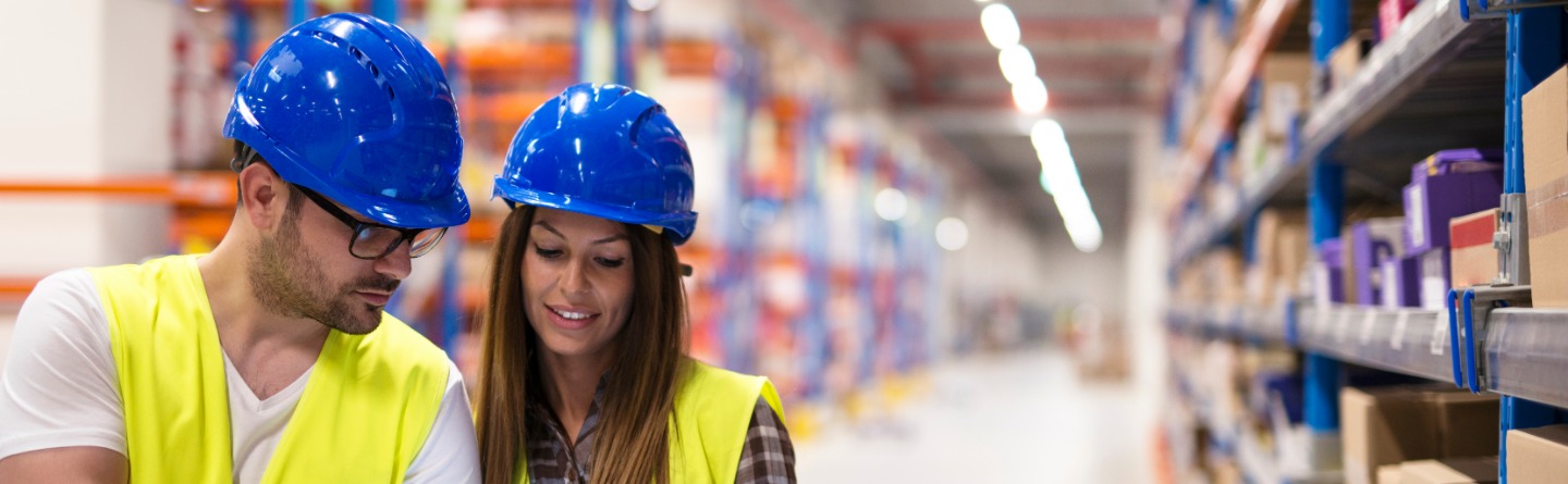 Header: Ein Mann und eine Frau in Arbeitskleidung im Materiallager