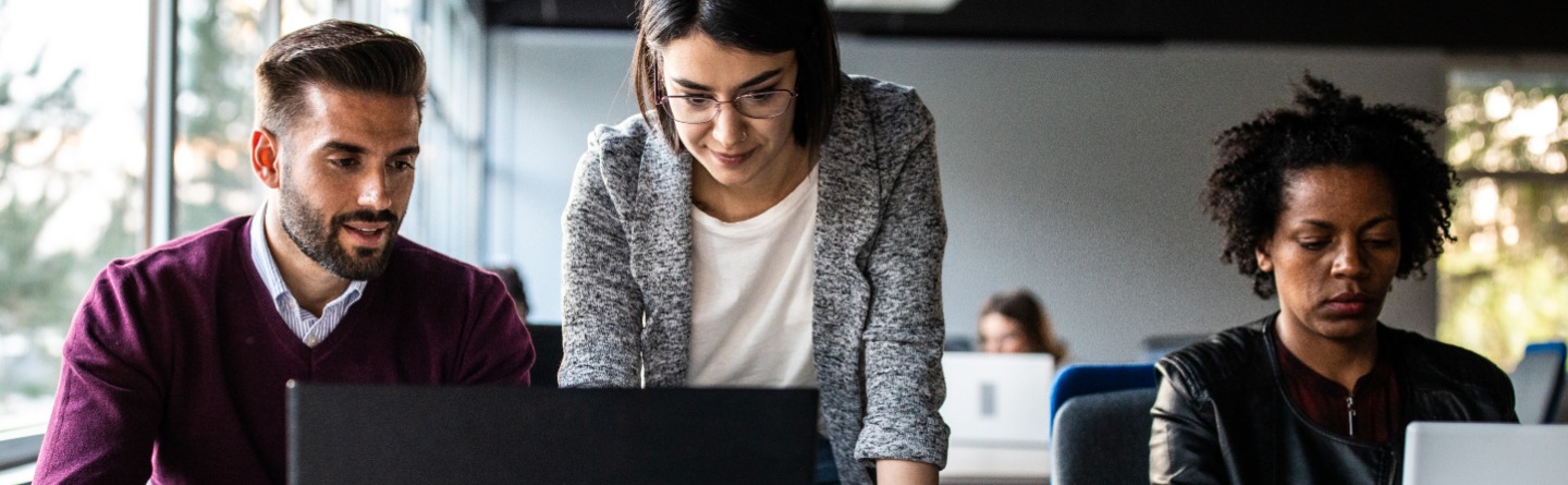 Header: Zwei Personen vor einen Laptop in einer Schulungssituation.