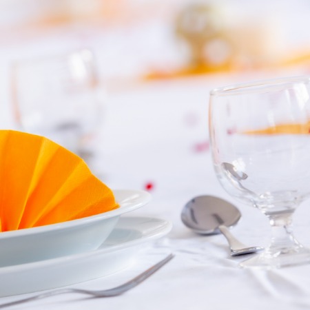 Anschnitt eingedeckter Tisch mit weißem Geschirr und orangefarbener Serviette