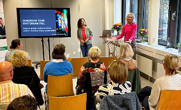 Zwei Frauen stehen vorn auf der Bühne neben Bildschirm